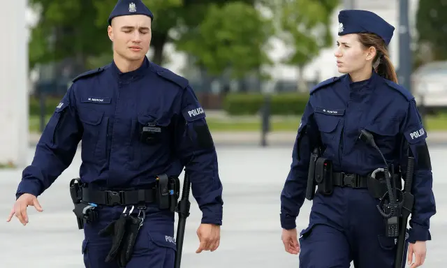 Dwóch policjantów w granatowych mundurach, mężczyzna i kobieta, idzie w stronę widza.