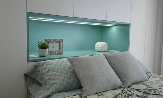 Habitación verde pistacho y gris con cama, almohadas y nicho iluminado.