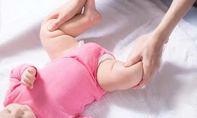 Delikatne badanie nóżek niemowlaka, uwaga skupiona na asymetrii fałdów udowych.