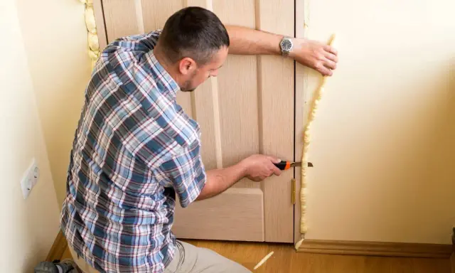 Hombre corta poliuretano expandido sobrante alrededor de un marco de puerta.
