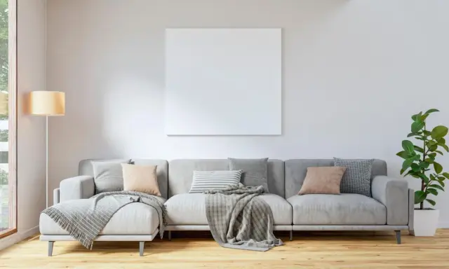 Sofá gris con cojines en tonos tierra y grises, mantas y planta. El color de cojines para sofá gris ideal para un ambiente acogedor.