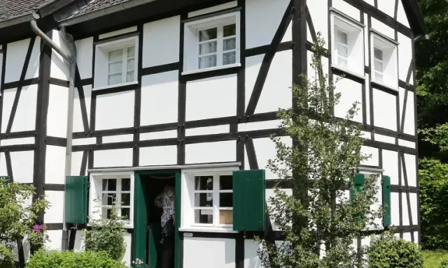 Ein liebevoll saniertes Fachwerkhaus mit grünen Fensterläden und üppiger Bepflanzung.