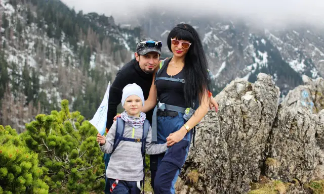 Rodzina na tle górskiej panoramy. Dziecko z flagą stoi na sarniej skale, obok rodzice.