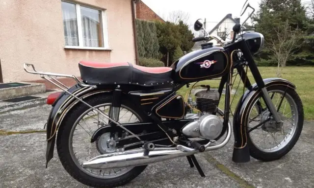 Czarny motocykl z PRL-u, z czerwonym siedzeniem i złotymi ozdobami. Klasyka polskich motocykli.
