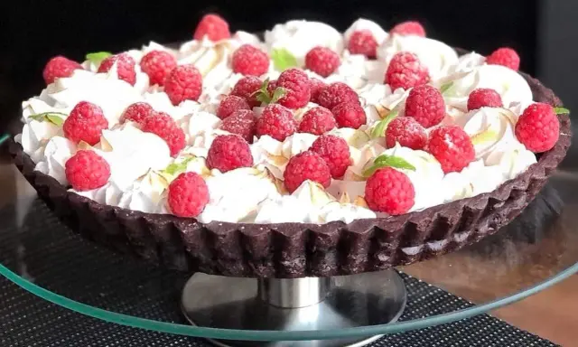 Pyszna tarta czekoladowa z malinami, udekorowana bitą śmietaną i listkami mięty. Idealna na deser.