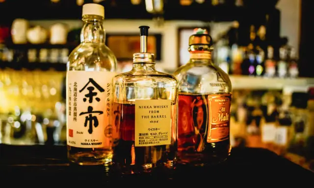 Tre flaskor japansk sprit, inklusive Nikka Whisky From The Barrel och Yoichi, står uppradade på en mörk yta.