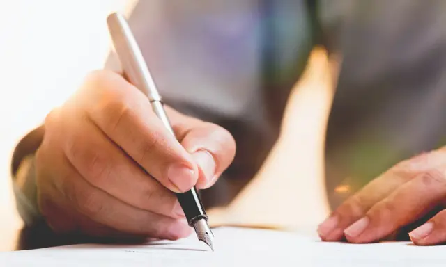 Dłoń pisze piórem po papierze, przygotowując dokument. Dowiedz się, jak napisać testament.