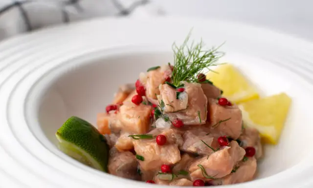Un classique tartare de saumon, frais et coloré, garni d'aneth, de baies roses et servi avec des quartiers de citron vert et de citron jaune.