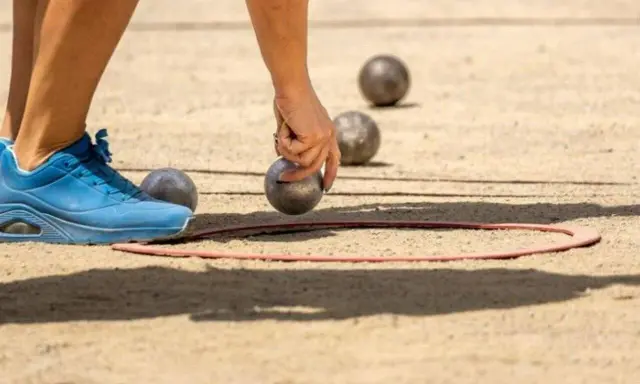 Une main saisit une boule de pétanque, prête à la lancer dans le cercle. Les règles du jeu de boules sont simples : viser le cochonnet.