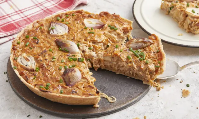 Une délicieuse tarte à l'oignon, garnie d'oignons caramélisés et de ciboulette fraîche, est prête à être dégustée. Une part est servie sur une assiette.
