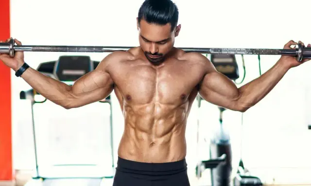 Ein Mann mit stark definierten Bauchmuskeln hält eine Langhantel im **cutten gym**.