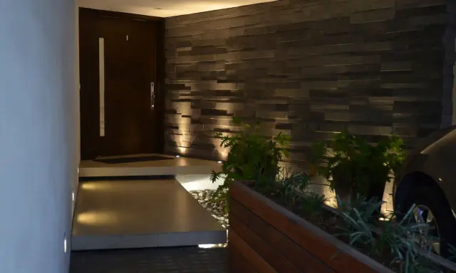 Ingresso con gradino interno illuminato, porta scura, muro in pietra e piante.