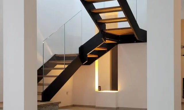 Scala interna con gradini in legno e struttura metallica nera. Il parapetto in vetro trasparente dona leggerezza al design moderno.