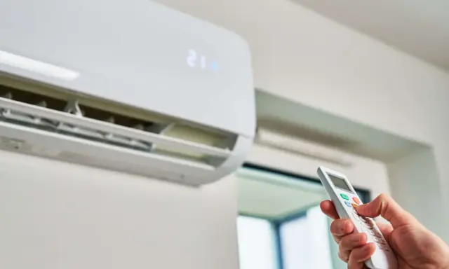 Mano ajustando el aire acondicionado a la temperatura ideal para ahorrar energía. La unidad muestra 21 grados.