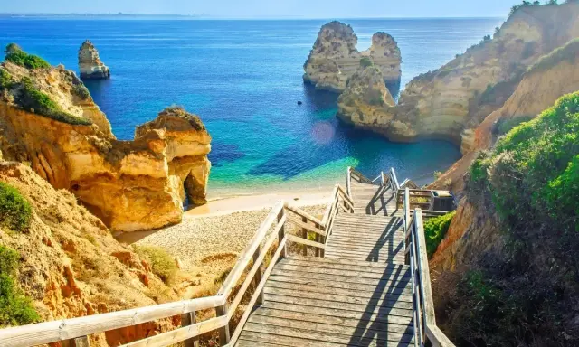 Malownicze schody prowadzą do ukrytej plaży z turkusową wodą, otoczonej klifami. Idealne miejsce na wakacje w portugalskich miastach turystycznych.