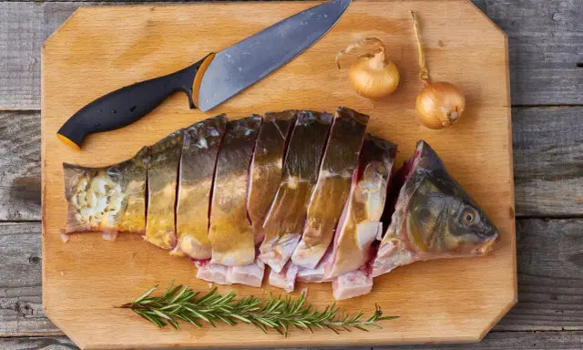 Pokrojony karp, cebula i rozmaryn na desce. Idealne składniki na pyszny groszek karpia.