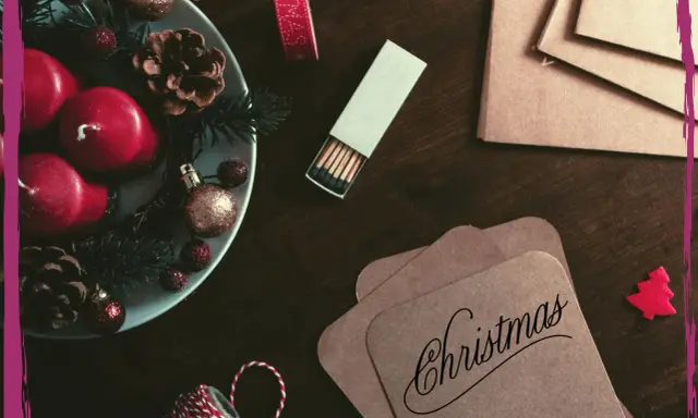 Candele rosse, pigne e decorazioni natalizie su un tavolo scuro, pronte per scrivere una poesia di Natale per adulti.