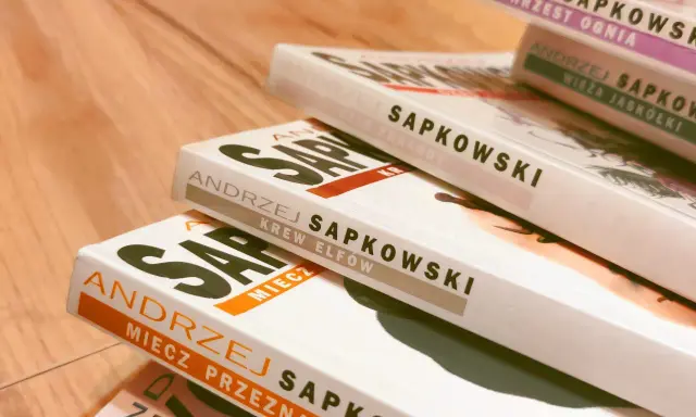 Stos książek Andrzeja Sapkowskiego, idealny przewodnik, jak czytać Wiedźmina. Widoczne tytuły: "Chrzest Ognia", "Wieża Jaskółki", "Czas Pogardy", "Krew Elfów", "Miecz Przeznaczenia".