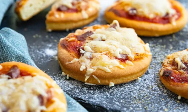 Mehrere mini pizza mit geschmolzenem Käse und Tomatensauce auf einem dunklen Untergrund, bestreut mit etwas Mehl.