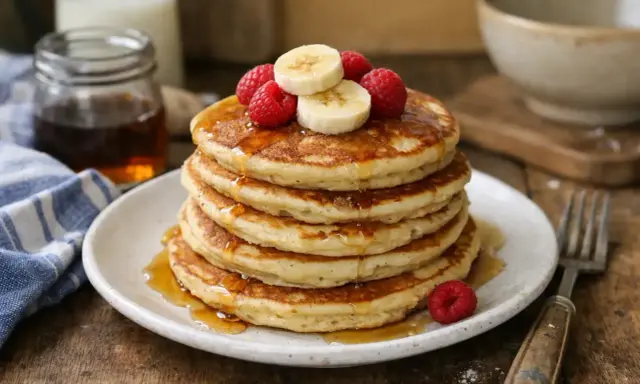 Pile de pancakes sans oeuf, garnis de framboises et rondelles de banane, arrosés de sirop d'érable. Un délice pour le petit-déjeuner.