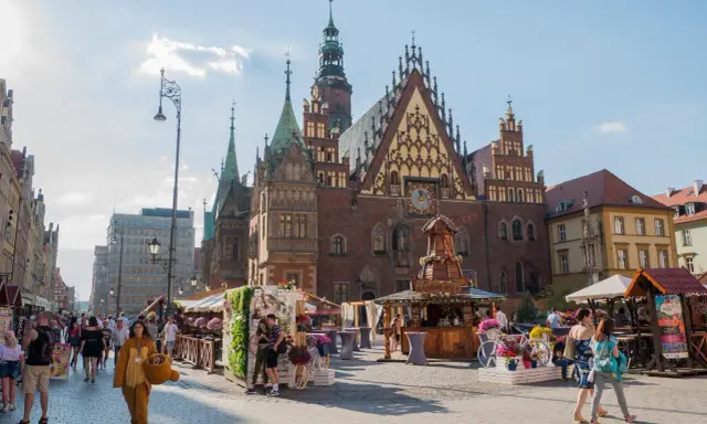 Wrocław stare miasto tętni życiem. Ludzie spacerują po Rynku, podziwiając zabytkowy ratusz i kolorowe kramy.