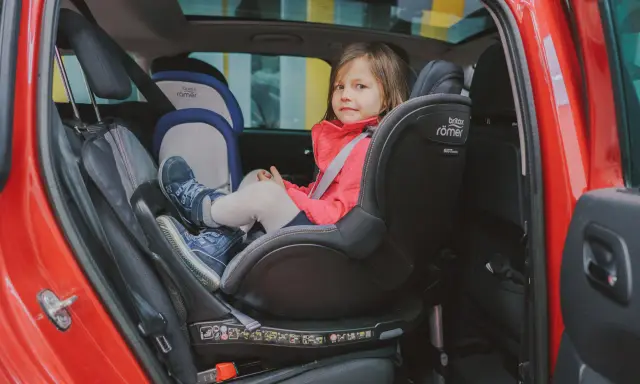 Mała dziewczynka w czerwonej kurtce siedzi w foteliku samochodowym Britax Römer.