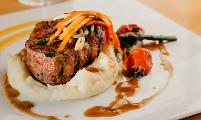Un plat de viande grillée, purée de pommes de terre et légumes, une des spécialités d'Aurillac, servi sur une assiette blanche avec une sauce brune.