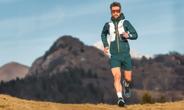 Ein Mann läuft in den Bergen, was ist ein ultramarathon? Er trägt Laufkleidung und eine Weste.