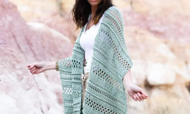Mujer con gafas de sol luciendo un chaleco de **mantones de crochet** verde menta, con un diseño calado y mangas anchas, sobre una camiseta blanca y pantalones beige.