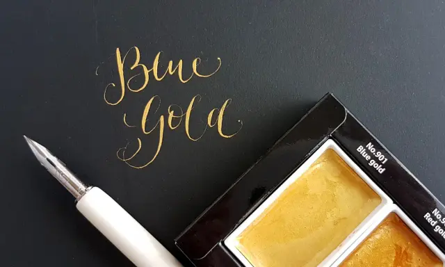 Złoty napis "Blue Gold" obok pióra i palety farb.