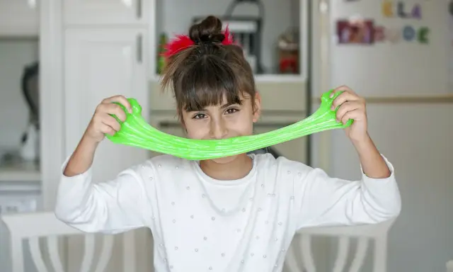 Bambina sorridente con slime verde brillante, un divertente esperimento per la ricetta slime fatta in casa.