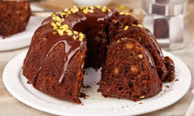 Pyszna babka na oleju, polana czekoladą i posypana pistacjami, z kawałkiem na talerzyku.