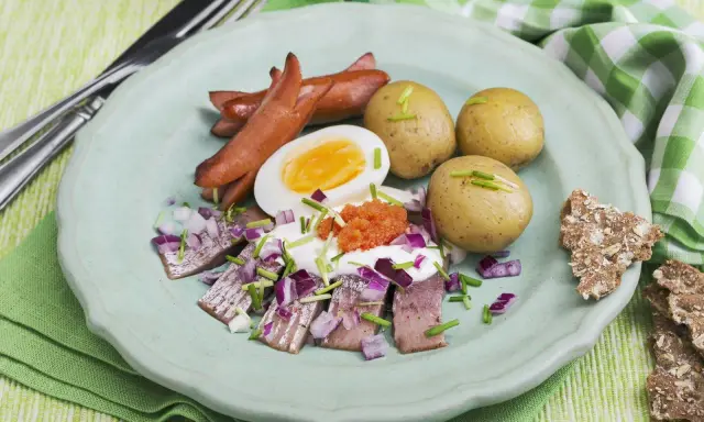 En tallrik med sill, ägg, korv och potatis. En klassisk del av ett svenskt påskbord med mat som passar alla.