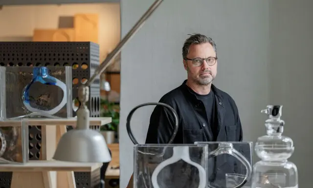 Matti Klenell, en man med glasögon, står bland sina konstverk av glas.
