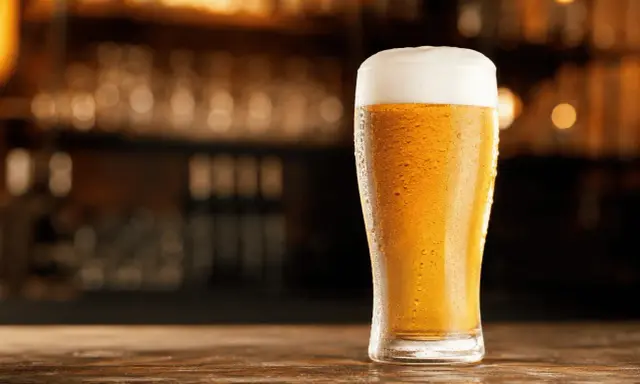 Schłodzony pilsner z obfitą pianką na blacie drewnianego baru.
