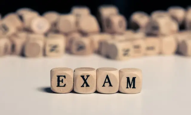 Drewniane kostki z literami tworzą napis "EXAM". Zastanawiasz się, na jakim poziomie jest matura podstawowa z angielskiego?