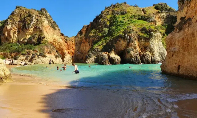 Sonnige Bucht mit Felsen und türkisfarbenem Wasser. Menschen baden und genießen das milde Wetter im **Portugal im Dezember**.