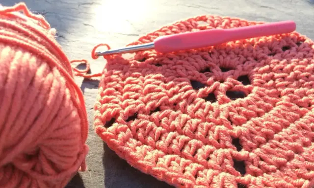 Koralowa włóczka i szydełko tworzą wzór. Powstaje piękny, ażurowy crochet pattern.