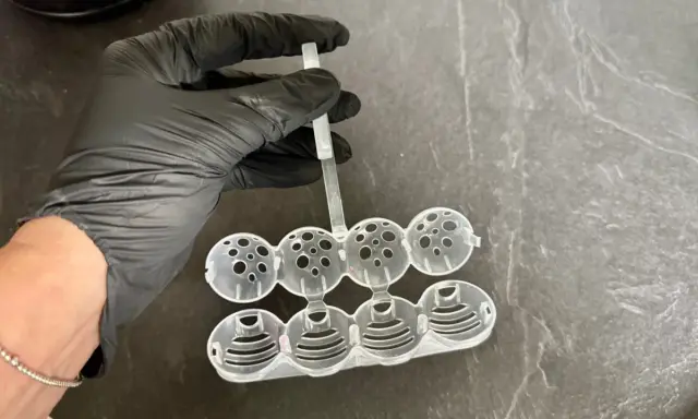 Hand in black glove holds a mold for making klostein selber machen. The mold has eight spherical compartments.