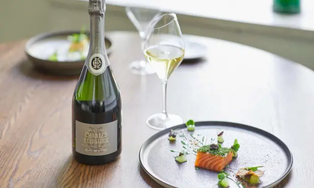 Flasche Charles Heidsieck Champagner neben Lachs mit Kaviar auf einem Teller.