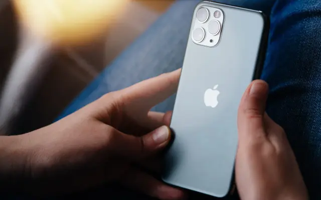 Dłonie trzymające szare iPhone'a z widocznym logo Apple i modułem aparatów.