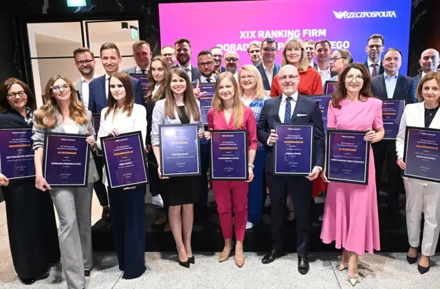 Grupa osób w eleganckich strojach pozuje z dyplomami na tle sceny z logo "Rzeczpospolita".