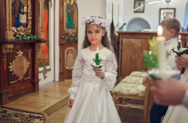 Dziewczynka w białej sukni i wianku trzyma świecę. To ważny dzień, w której klasie komunia?