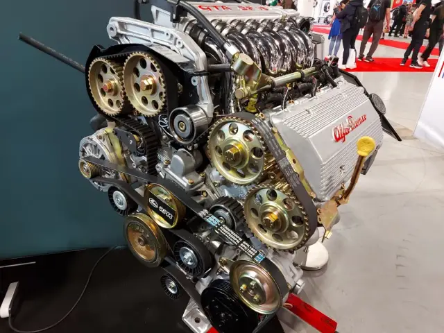 Silnik Alfa Romeo z widocznym układem rozrządu, kołami zębatymi i paskami. Widać napis "GTA 16V" i logo producenta. To serce potężnej maszyny, być może z legendarnym silnikiem hemi.
