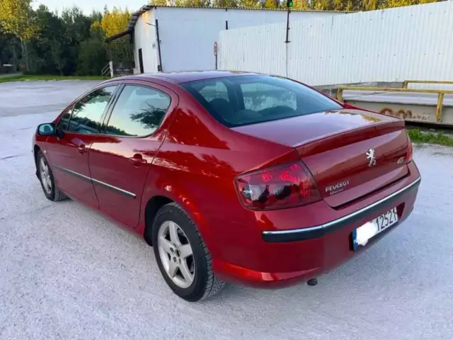 Błyszczący czerwony Peugeot 407 2.0 HDI z przyciemnianymi szybami stoi na żwirowym podjeździe.