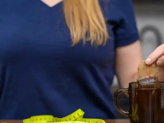 Kobieta zanurza torebkę herbaty w kubku, obok leży miarka. Czy nerki można wygrzewać?