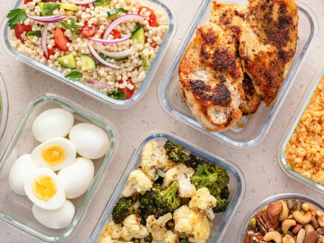 Förberedd student mat i glasbehållare: kycklingfilé, couscoussallad, grönsaker, ägg och nötter. Perfekt för en hälsosam lunchlåda.