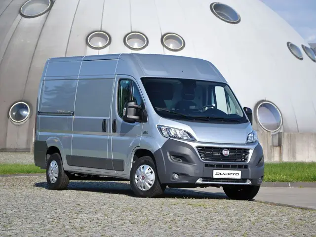 Srebrny Fiat Ducato 2.3 Multijet zaparkowany przed futurystycznym budynkiem z okrągłymi oknami.