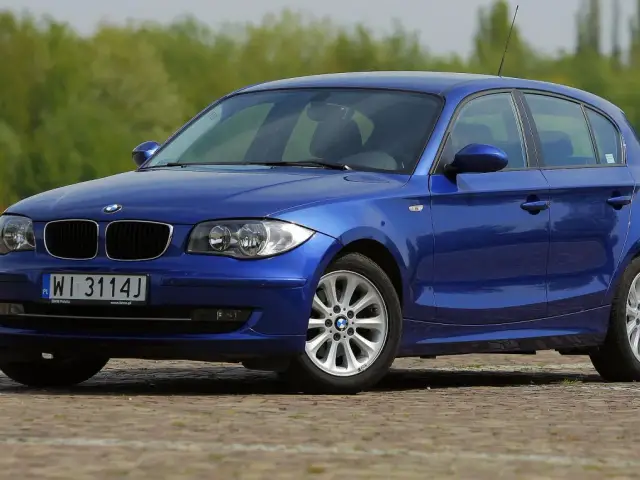 Niebieskie BMW 118i na tle zieleni. Elegancki hatchback z polskimi tablicami rejestracyjnymi WI 3114J.