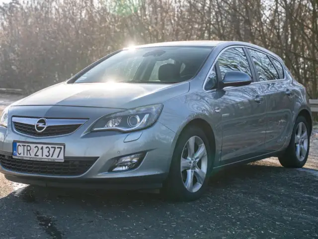 Szary Opel Astra z silnikiem 1.7 cdti zaparkowany na poboczu drogi, w tle drzewa i słońce.